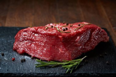 Çiğ et dana biftek siyah üzerine kurulu baharat ve biberiye ile ahşap arka plan üzerinde kopya alanı kayrak