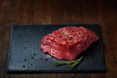 Çiğ et dana biftek siyah üzerine kurulu baharat ve biberiye ile ahşap arka plan üzerinde kopya alanı kayrak