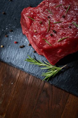 Çiğ et dana biftek siyah üzerine kurulu baharat ve biberiye ile ahşap arka plan üzerinde kopya alanı kayrak