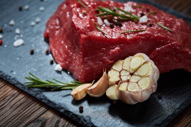 Çiğ et dana biftek siyah üzerine kurulu baharat, sarımsak ve biberiye ile ahşap arka plan üzerinde seçici odak kayrak