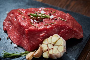 Çiğ et dana biftek siyah üzerine kurulu baharat, sarımsak ve biberiye ile ahşap arka plan üzerinde seçici odak kayrak