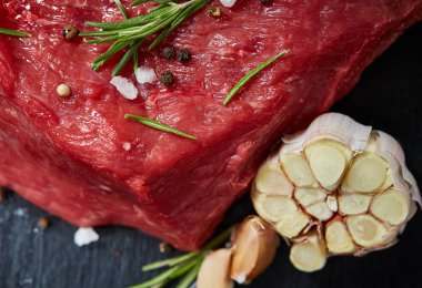 Çiğ et dana biftek siyah üzerine kurulu baharat, sarımsak ve biberiye ile ahşap arka plan üzerinde seçici odak kayrak