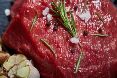 Çiğ et dana biftek siyah üzerine kurulu baharat, sarımsak ve biberiye ile ahşap arka plan üzerinde seçici odak kayrak