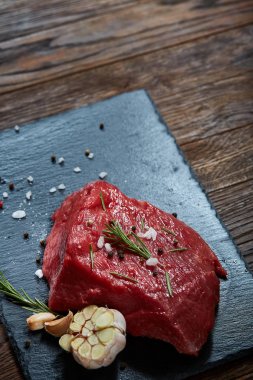 Çiğ et dana biftek siyah üzerine kurulu baharat, sarımsak ve biberiye ile ahşap arka plan üzerinde seçici odak kayrak