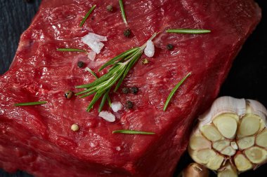 Çiğ et dana biftek siyah üzerine kurulu baharat, sarımsak ve biberiye ile ahşap arka plan üzerinde seçici odak kayrak