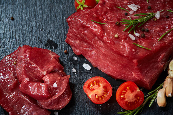 Composition of raw beefsteak on slate board with vegetables and seasoning, selective focus, close-up.