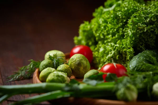 Vegetarian still life of fresh vegetables on wooden plate over rustic background, close-up, flat lay. — Stock Photo, Image