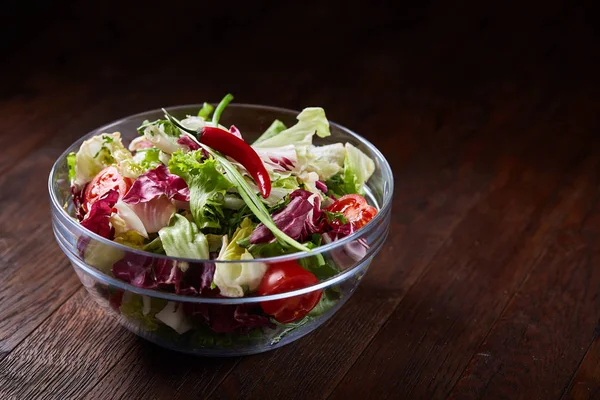 Salada de legumes frescos servida em tigela de vidro sobre fundo de madeira escura, foco seletivo, profundidade rasa de campo — Fotografia de Stock