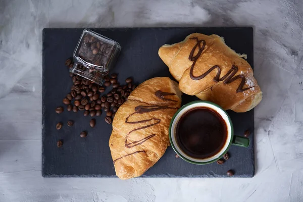 Coffee cup, jar with coffee beans, croissants on stone board over white background, selective focus, close-up — Stock Photo, Image