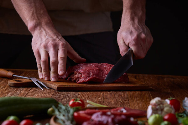 Strong professional mans hands cutting raw beefsteak, selective focus, close-up