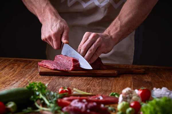 Strong professional mans hands cutting raw beefsteak, selective focus, close-up