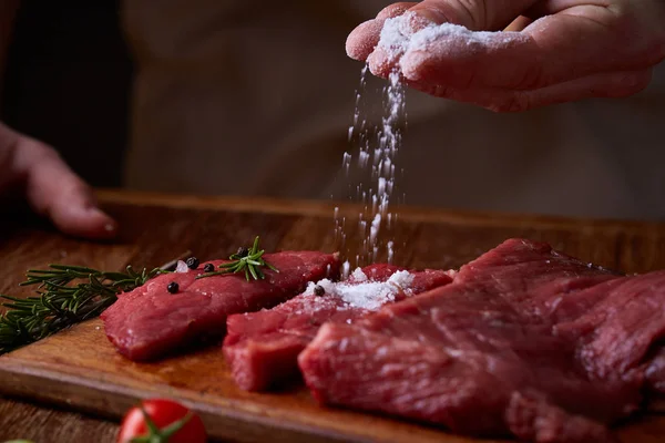 Strong professional mans hands spilling salt on raw beefsteak, selective focus, close-up