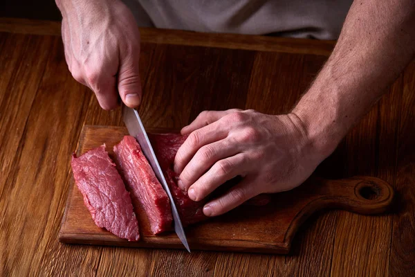 Forti mani professionali di mans che tagliano la bistecca cruda, messa a fuoco selettiva, primo piano Fotografia Stock