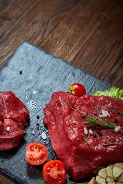 Çiğ et dana biftek siyah üzerine kurulu baharat, sarımsak ve biberiye ile ahşap arka plan üzerinde seçici odak kayrak