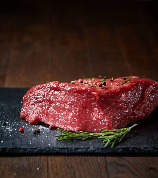 Çiğ et dana biftek siyah üzerine kurulu baharat ve biberiye ile ahşap arka plan üzerinde kopya alanı kayrak — Stok fotoğraf