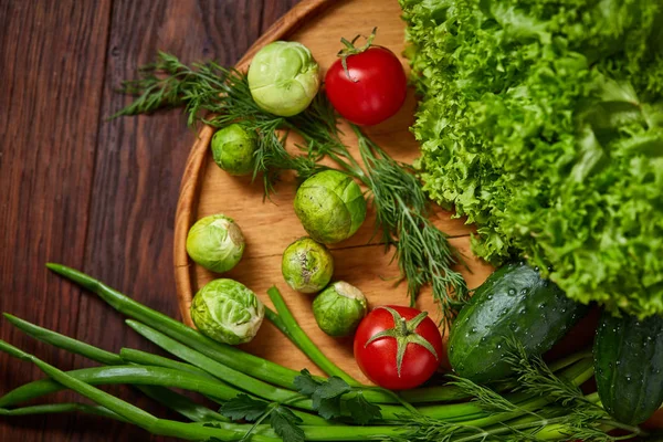 Nature morte végétarienne de légumes frais sur assiette en bois sur fond rustique, gros plan, plat . — Photo