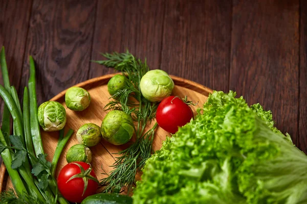 Nature morte végétarienne de légumes frais sur assiette en bois sur fond rustique, gros plan, plat . — Photo