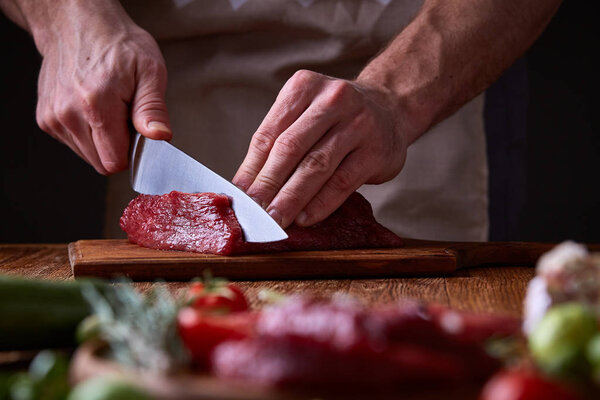 Strong professional mans hands cutting raw beefsteak, selective focus, close-up