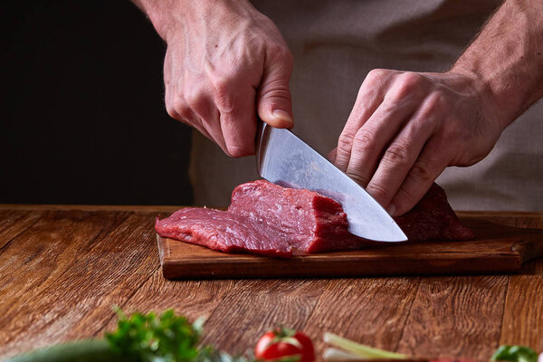 Strong professional mans hands cutting raw beefsteak, selective focus, close-up