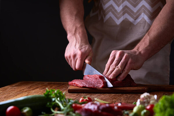 Strong professional mans hands cutting raw beefsteak, selective focus, close-up