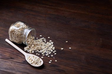 Devrilmiş cam kavanoz ve kaşık vintage ahşap arka plan, yakın çekim, seçici odak çiğ yulaf ezmesi ile.