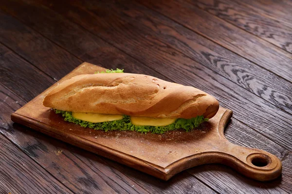 Sandwich fresco y sabroso con queso y verduras en tabla de cortar sobre fondo de madera, enfoque selectivo . — Foto de Stock
