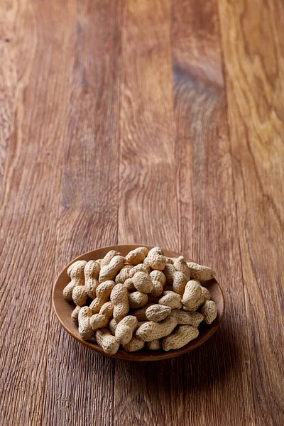 Unpeeled peanuts in wooden bowl over rustic wooden background closeup, selective focus