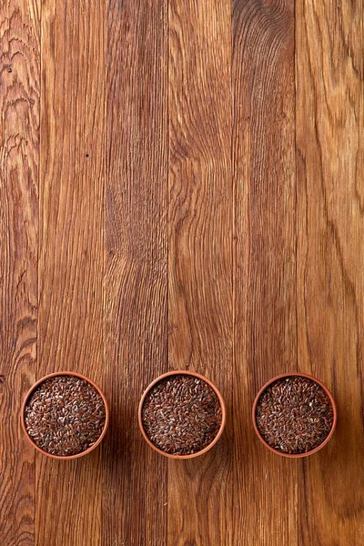 Tres cuencos de cerámica con semillas de lino dispuestos en fila sobre fondo de madera, vista superior, enfoque selectivo — Foto de Stock