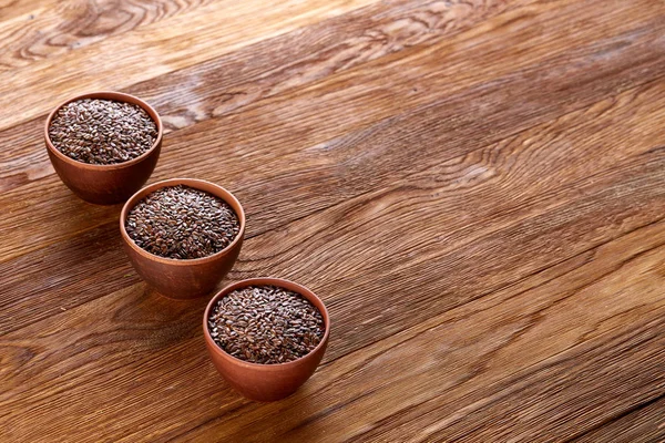 Tres cuencos de cerámica con semillas de lino dispuestos en fila sobre fondo de madera, vista superior, enfoque selectivo — Foto de Stock