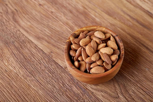 Bowl of almonds on wooden background, top view, close-up, selective focus. — Stock Photo, Image
