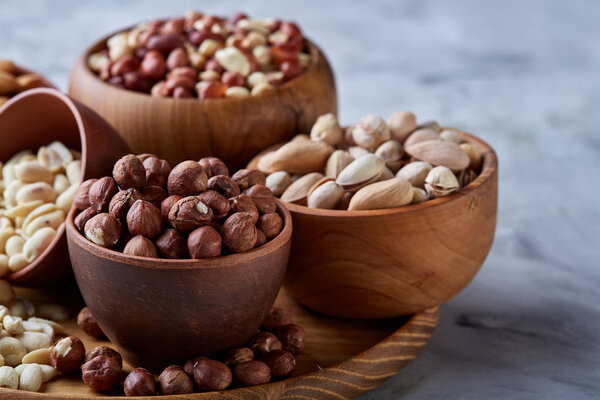 Mixed nuts in brown bowls on wooden tray over white background, close-up, top view, selective focus.