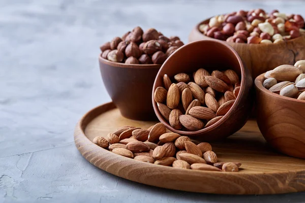 Mixed nuts in brown bowls on wooden tray over white background, close-up, top view, selective focus.