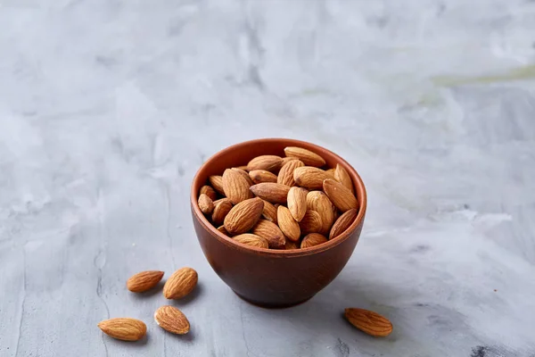 Bowl of almonds on white textured background, top view, close-up, selective focus.