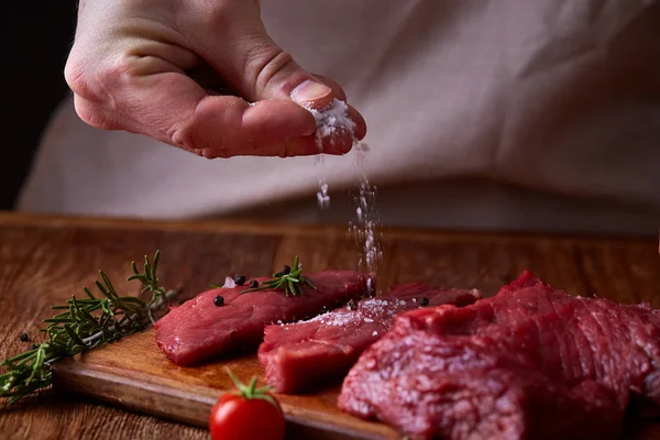 Strong professional mans hands spilling salt on raw beefsteak, selective focus, close-up