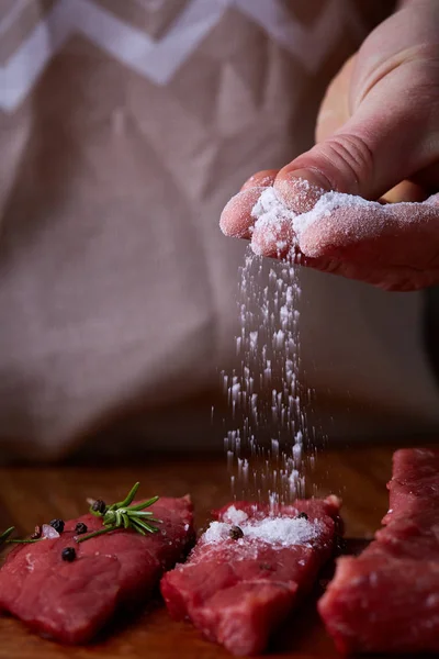 Strong professional mans hands spilling salt on raw beefsteak, selective focus, close-up