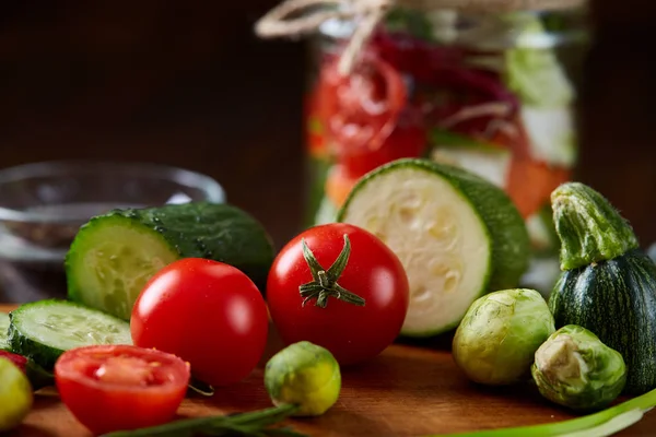 Pyszne sałatki warzywne w słoiku i świeże warzywa na deska do krojenia na stół, Selektywny fokus, zbliżenie — Zdjęcie stockowe