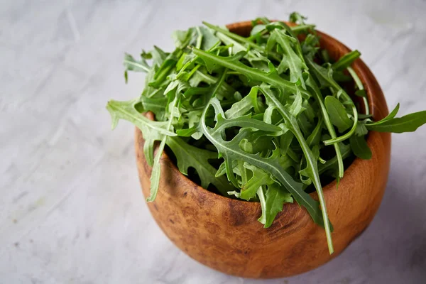 Ruccola proaspătă într-un castron de lemn pe fundal texturat alb, adâncime mică a câmpului . — Fotografie, imagine de stoc