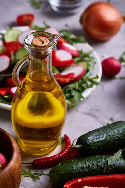 Delicious masih hidup dengan minyak zaitun emas dalam botol kaca di depan piring dengan salad sayuran — Stok Foto