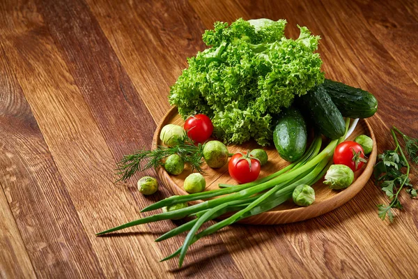 Nature morte végétarienne de légumes frais sur assiette en bois sur fond rustique, gros plan, plat . — Photo