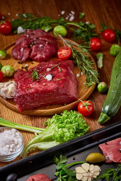 Still life of raw beef meat with vegetables on wooden plate over vintage background, top view, selective focus — Stock Photo, Image