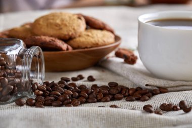 Kahve fincanı, kahve çekirdekleri, saf masa örtüsü, seçici odak, yakın çekim, yan görünümü kurabiye kavanozu