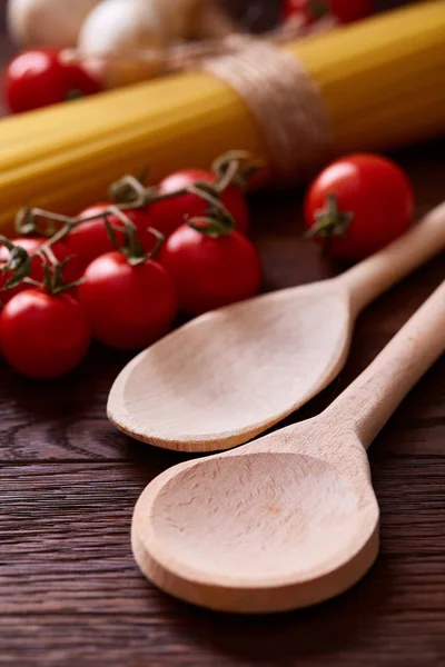 Uncooked pasta, tomatoes and two spoons on wooden background, top view, close-up, shallow depth of field — Stock Photo, Image