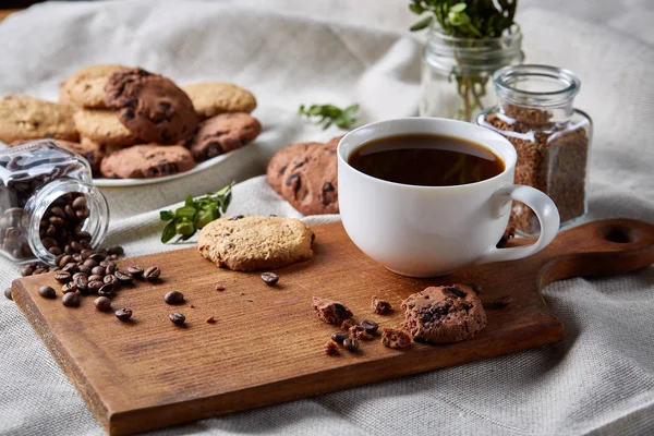 Taza de café, frasco con granos de café, galletas sobre mantel hecho en casa, enfoque selectivo, primer plano, vista superior — Foto de Stock