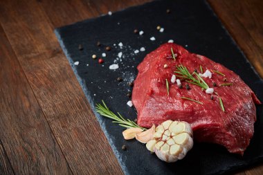 Çiğ et dana biftek siyah üzerine kurulu baharat, sarımsak ve biberiye ile ahşap arka plan üzerinde seçici odak kayrak