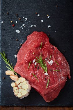 Çiğ et dana biftek siyah üzerine kurulu baharat, sarımsak ve biberiye ile ahşap arka plan üzerinde seçici odak kayrak