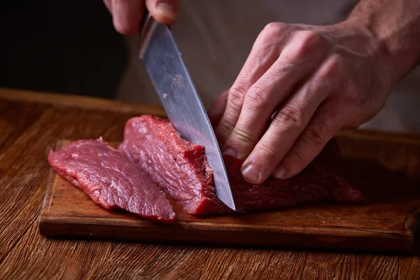 Strong professional mans hands cutting raw beefsteak, selective focus, close-up