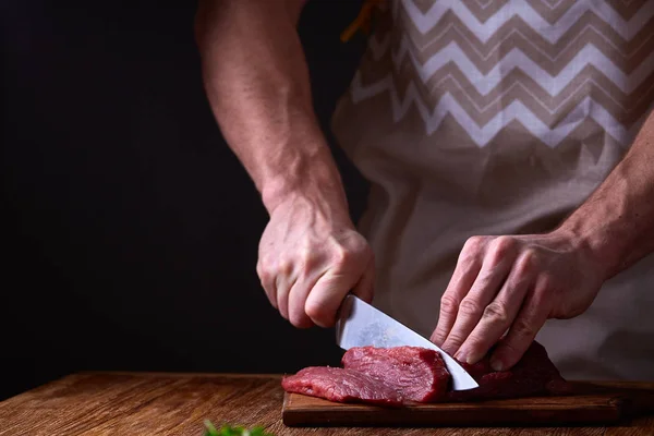 Strong professional mans hands cutting raw beefsteak, selective focus, close-up