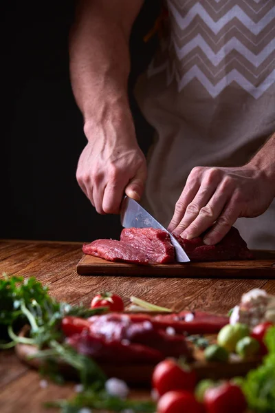 Strong professional mans hands cutting raw beefsteak, selective focus, close-up