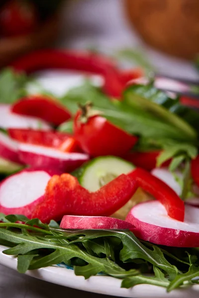 Kreatív friss növényi saláta, ruccola, uborka, paradicsom és retkek fehér tányérra, szelektív összpontosít — Stock Fotó