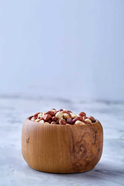 Cacahuetes mixtos crudos en placa de madera aislada sobre fondo texturizado blanco, vista superior, primer plano . — Foto de Stock